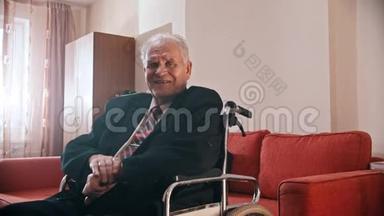 年迈的祖父-微笑的祖父坐在轮椅上看着摄像机